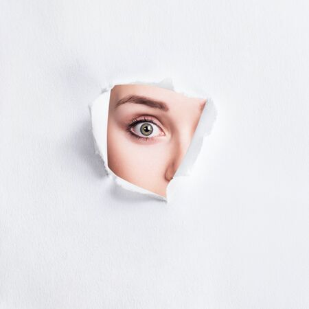 Surprised woman peeps into the slit of white paper.の写真素材
