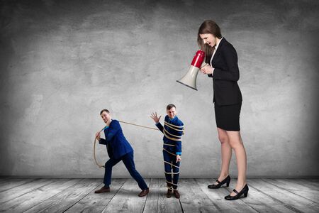Businesswoman gives orders and manager pulls tied himself.の写真素材