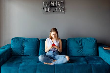 Young woman at home relaxing on the couch, using smartphone.の写真素材