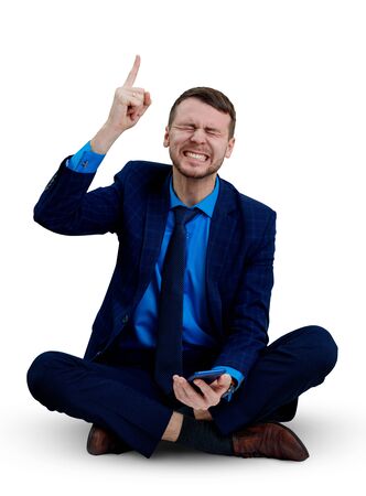Young angry businessman sitting on the floor with smartphone.の写真素材