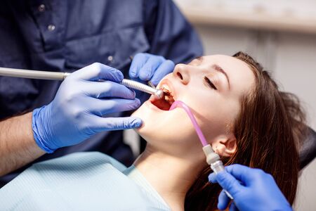 Male dentist treating teeth to young woman patient in clinic.の写真素材