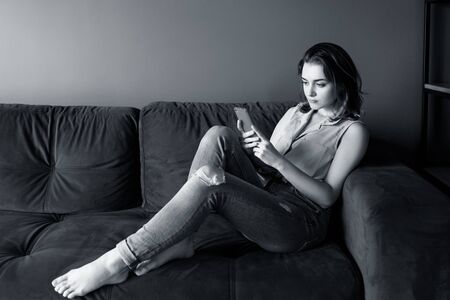 Young woman at home relaxing on the couch, using smartphone.の写真素材