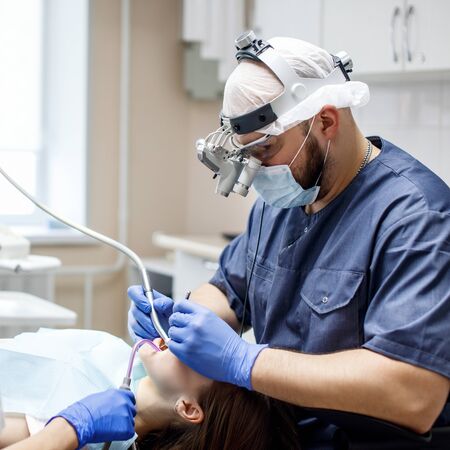 Male dentist treating teeth to young woman patient in clinic.の写真素材