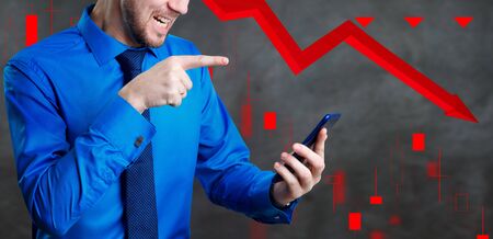 Businessman holds smartphone over gray background with red arrow downの写真素材