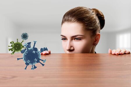 Woman with suspicion looks on coronavirus under the edge of table.の写真素材