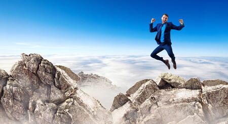 Young businessman feels success and jumps up over mountainsの写真素材