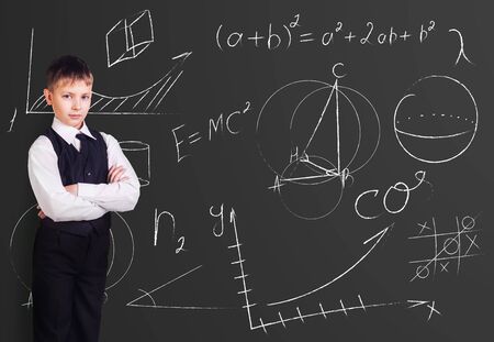 Little boy stands over blackboard background with formulas.の写真素材
