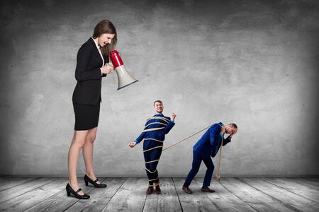 Businesswoman gives orders and manager pulls tied himself.の写真素材