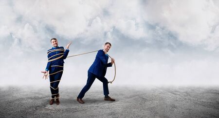 Angry businessman pulls tied himself with a rope.の写真素材