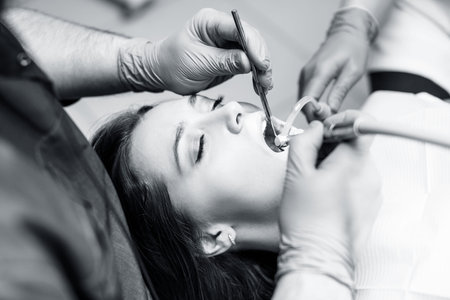 Dentist treating teeth to young woman patient in clinic.