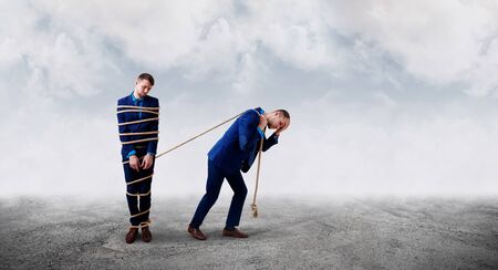 Upset businessman pulls tied himself with a rope. Over misty background outdoors.の写真素材