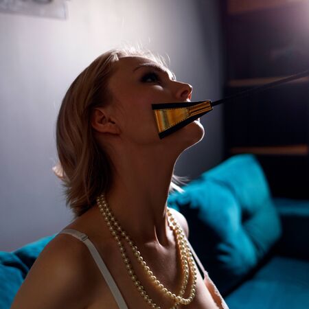 Blonde submissive woman sitting and leather whip touches her chin.の写真素材