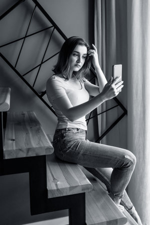 Young woman looks in smartphone and makes selfie on the staircase.