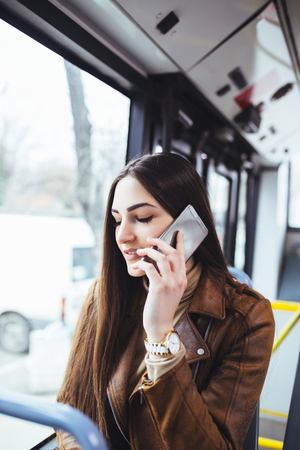 Beautiful young woman sitting in city bus and talking on mobile phone.の写真素材