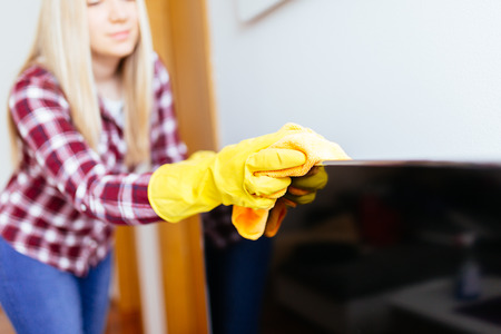 Beautiful young smiling woman cleaning TV with microfiber cloth.の写真素材