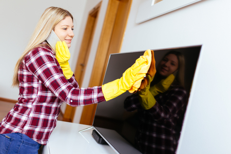 Beautiful young smiling woman cleaning house with microfiber cloth while talking on phone.の写真素材