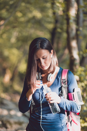Young woman in a forest opening a bottle of fresh water during an autumn walk.の写真素材