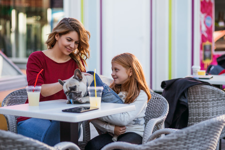 Mother and daughter enjoying with their French bulldog in cafeteria.の写真素材