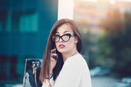 Business woman portrait outdoors talking at the phone with modern building as background.の写真素材