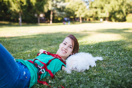 Portrait of beautiful smiling invalid young woman born without upper extremities enjoying with her little white puppy in park.の写真素材