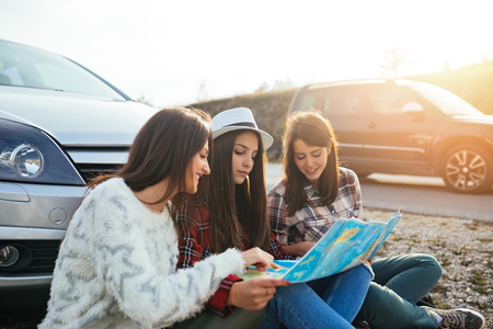 Friends sitting in front of their car and looking at map to find best route.の写真素材