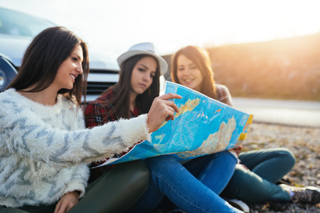 Friends sitting in front of their car and looking at map to find best route.の写真素材