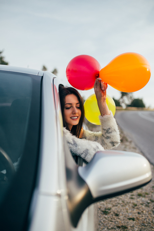 Young woman having fun while holding balloons through car window.の写真素材