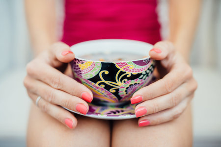 Women's hands with pink manicure holding a colorful cup of teaの写真素材