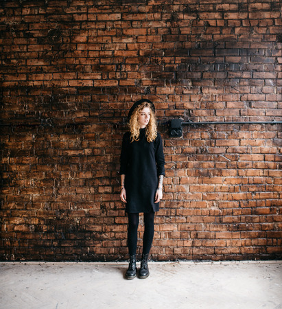 Beautiful curly girl in a bonnet standing against a brick wallの写真素材