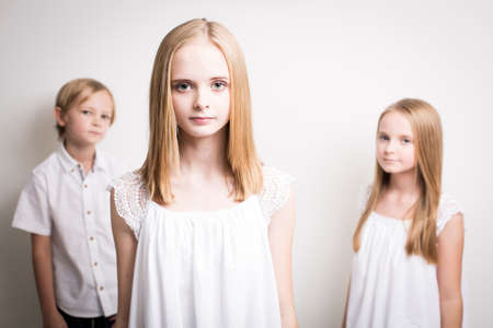 Studio shot with two girls and one boy all blond and all dressed in white clothing against a white background.の写真素材