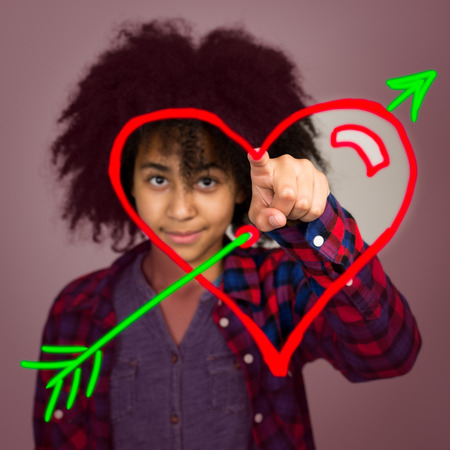A mixed race teenage girl with afro hairstyle drawing a love heart with arrow in the air.の写真素材