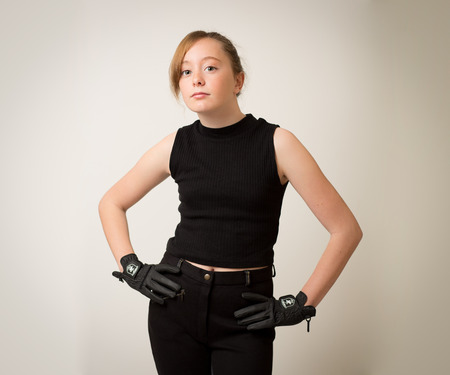Portrait of a beautiful teenage ginger girl with hair in a bun wearing a black horse riding outfit isolated against a grey background.の写真素材