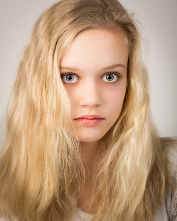 Studio portrait of a beautiful blond teenage girl with long hair and blue eyes isolated against a white background.の写真素材