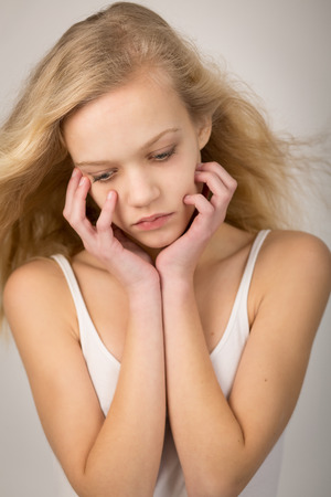Studio shot of a beautiful teenage girl with long hair blowing in the wind with her hands on her face looking down.の写真素材