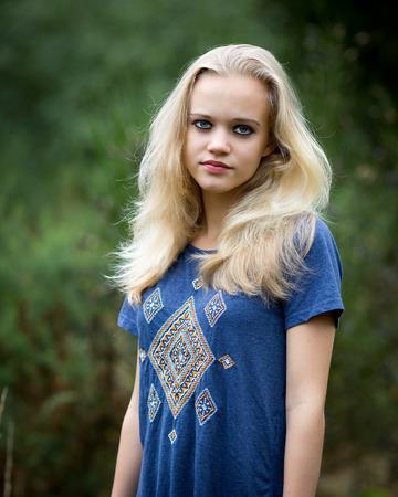 Location portrait of a beautiful blond teenage girl standing in a field having angel white long hair and wearing make-up and a blue top.の写真素材
