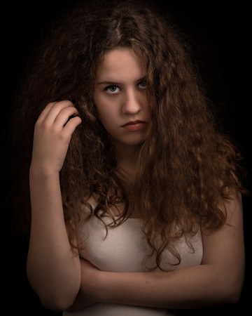 Studio portrait of a beautiful teenage woman with long thick curly ginger hair looking in the camera against an isolated background.の写真素材
