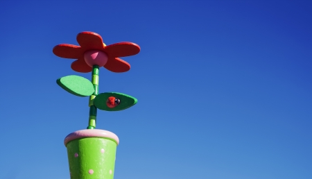 Close-up of a flower in a pot with a ladybug sitting on a leaf  Wooden Toy, shot against blue sky の写真素材