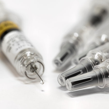 Syringe with vaccine to combat coronavirus on a table. A drop hangs from the tip of the needle.