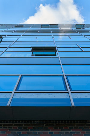 View upwards at the glass facade of a modern office building in Berlin with reflection of blue sky