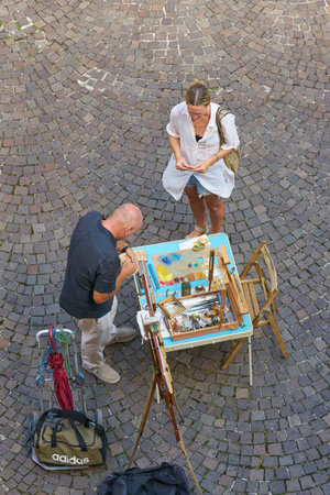 Malcesine, Italy â July 31, 2023: Holidaymaker in the old town of Malcesine in Italy buys a painted picture from a street artist as a souvenirのeditorial素材