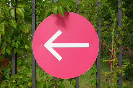 Sign with an arrow pointing left on a fence, indicating the right direction