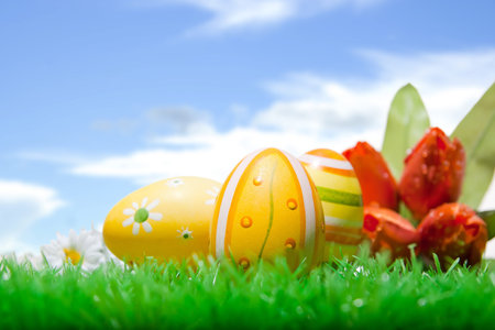 Closeup of three easter eggs on a well-kept lawn in front of blue cloudy sky