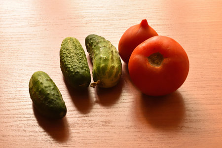 Vegetables tomatoes and cucumbers lie on a wooden boardの写真素材
