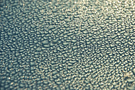 Close-up shot of dew drops on a light blue or turquoise metallic surface, glistening from the lightの写真素材