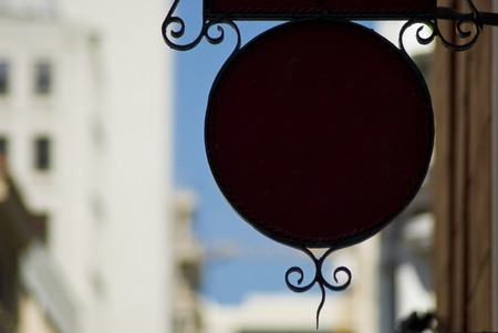 Black or dark circular sign hanging on the sidewlk, with buildings in the backgroundの写真素材