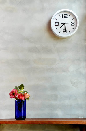 A photo of a clock and a blue vase with flowers の写真素材
