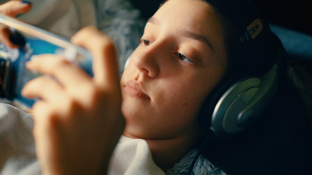 Young boy listening to music with headphones and smartphone lying in bed.の写真素材