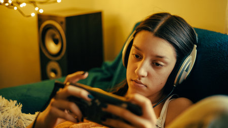Young woman in headphones playing video games on the sofa at home.の写真素材