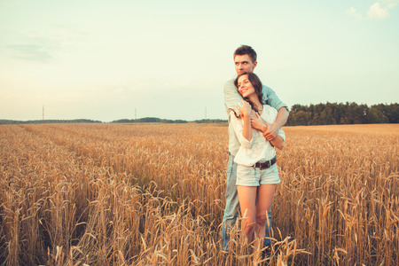 Young couple in love outdoor.d.Couple hugging.Young beautiful couple in love staying and kissing on the field on sunset. Soft sunny colors.の写真素材