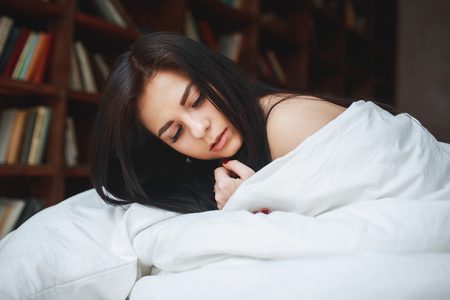 Sensual woman with dark hair lying on a bed at homeの写真素材
